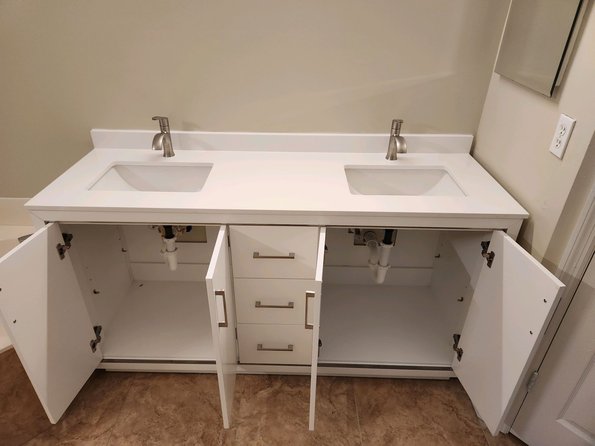 A white double-sink bathroom vanity with open cabinet doors and three central drawers in a light-colored room.
