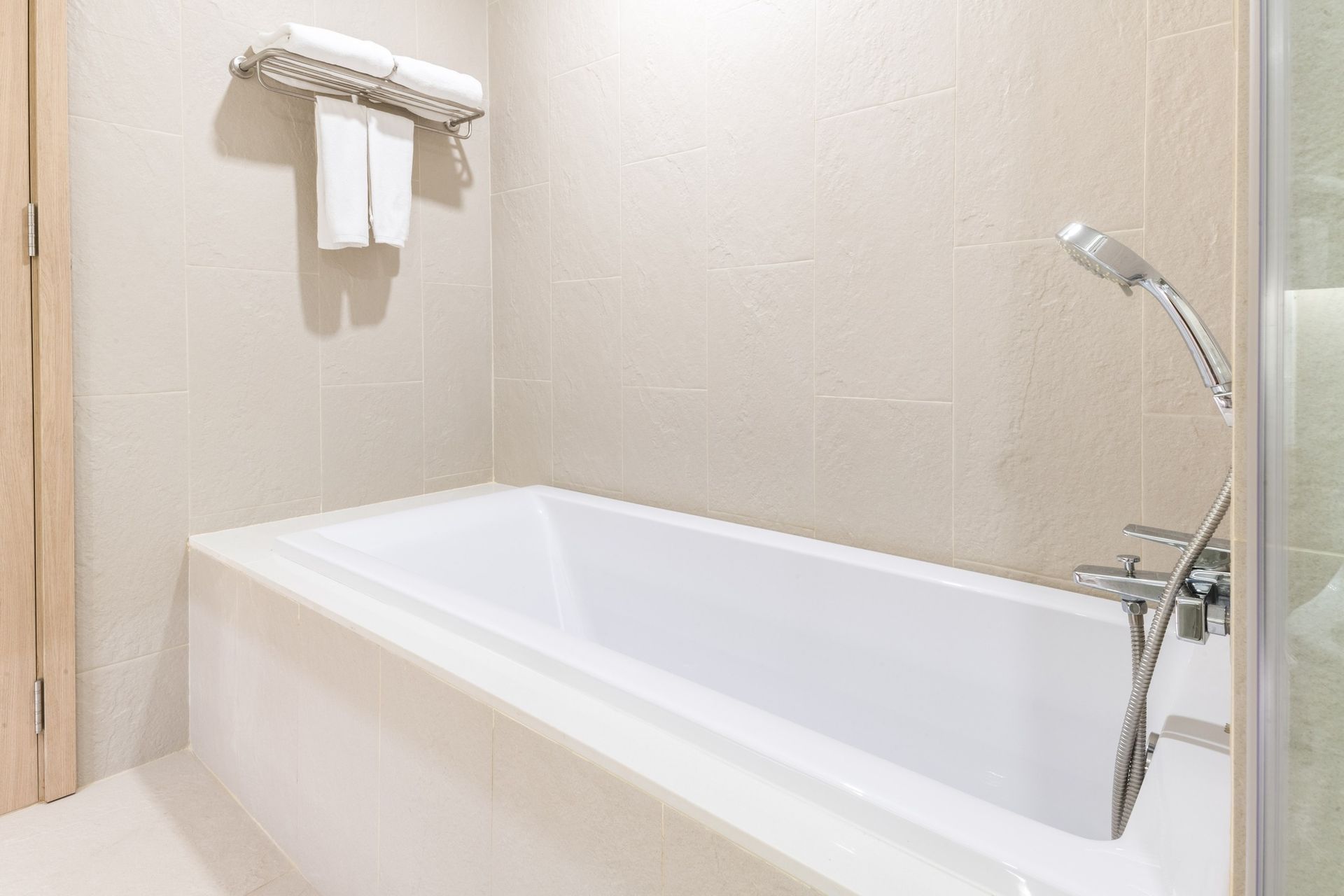A modern white bathtub in a bathroom with beige tiled walls and hanging white towels.