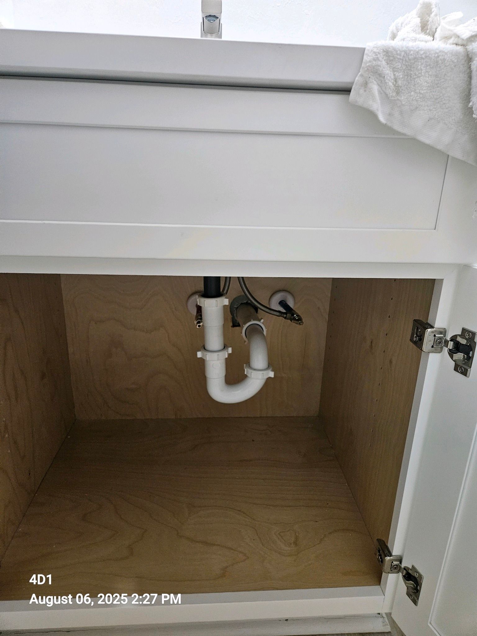 White bathroom vanity cabinet interior with plumbing pipes visible under a sink.