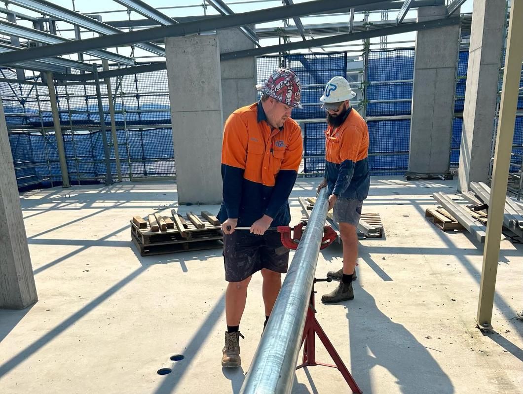 Two Construction Workers Cutting Metal Tubing on a Job Site — Nambucca Plumbing in Kempsey, NSW