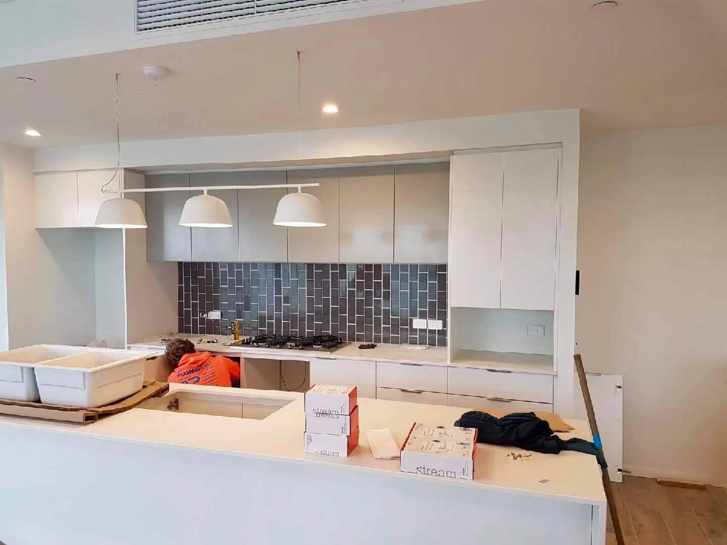 A Man Is Working in A Kitchen with White Cabinets and A Sink — Nambucca Plumbing in Nambucca Heads, NSW