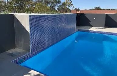 A Large Swimming Pool with Blue Tiles and A Black Wall Surrounding It — Nambucca Plumbing in Nambucca Heads, NSW