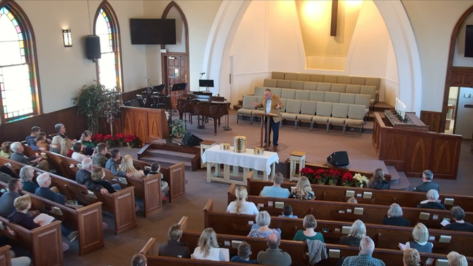 Congregation seated in a church sanctuary during a service, with the pastor at the front and choir seats behind.