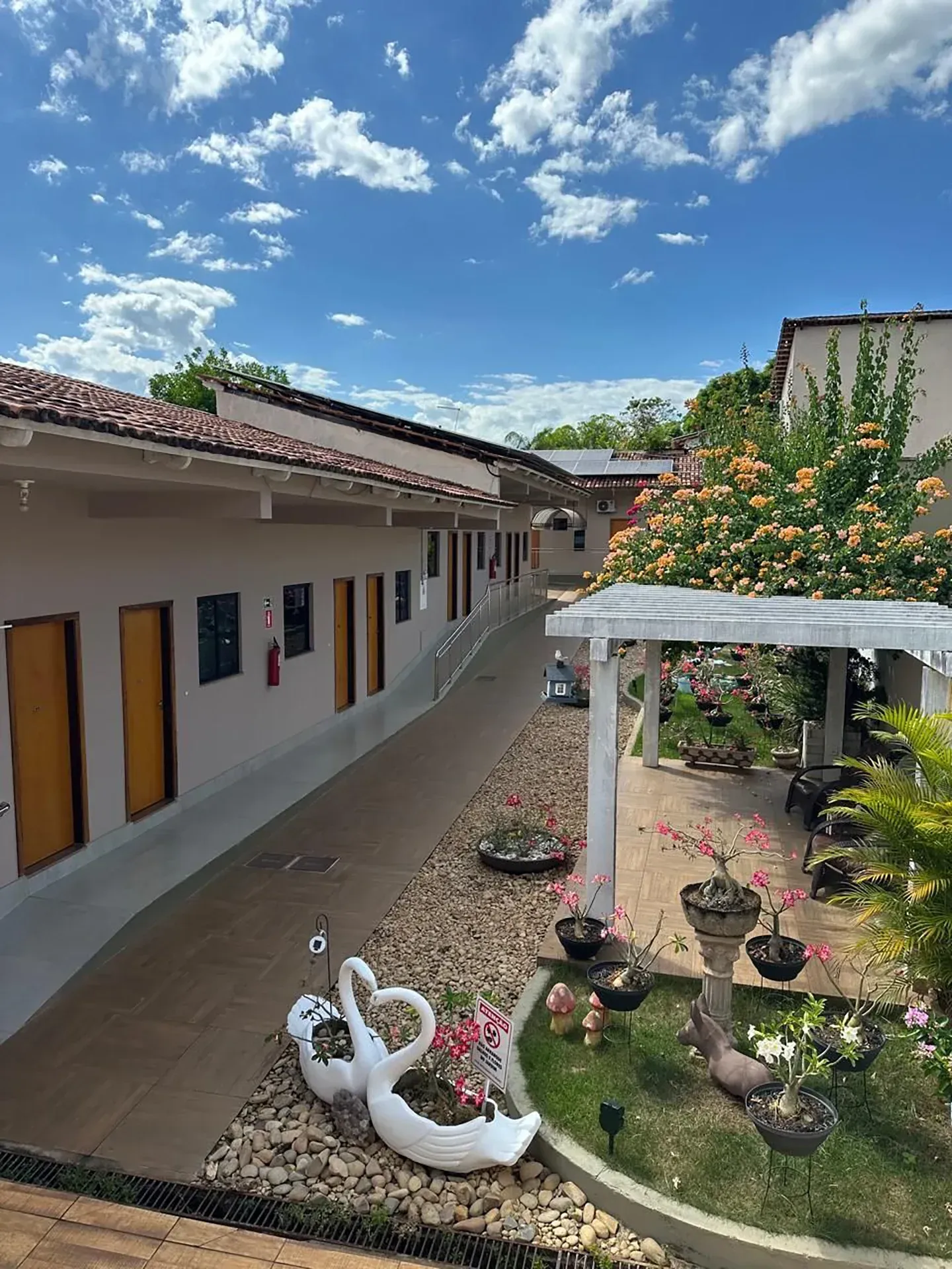 Pátio com edifícios brancos, passarelas e flores sob um céu azul.