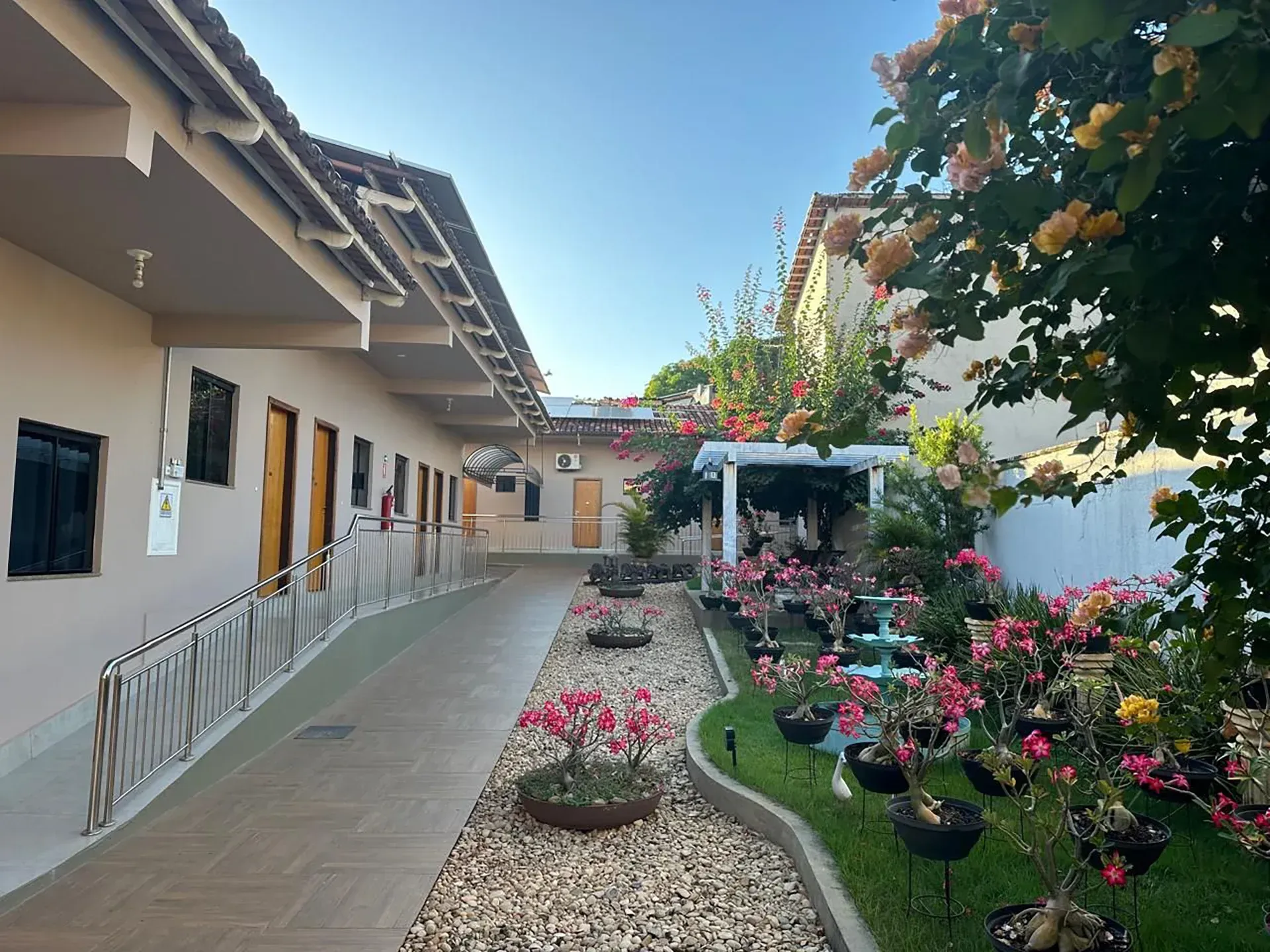 Pátio com edifícios brancos, passarelas e flores sob um céu azul.