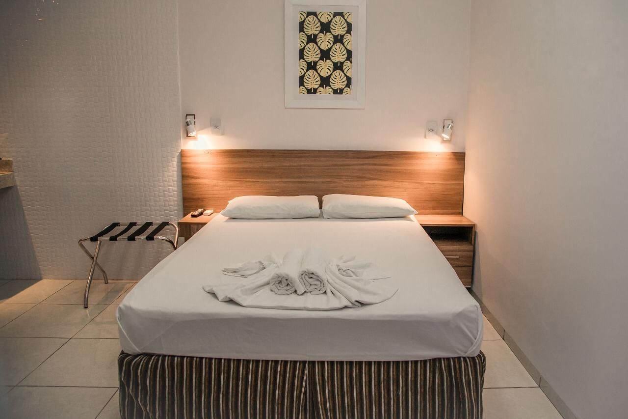 Quarto de hotel com cama, mesas de cabeceira, obras de arte e um porta-malas.