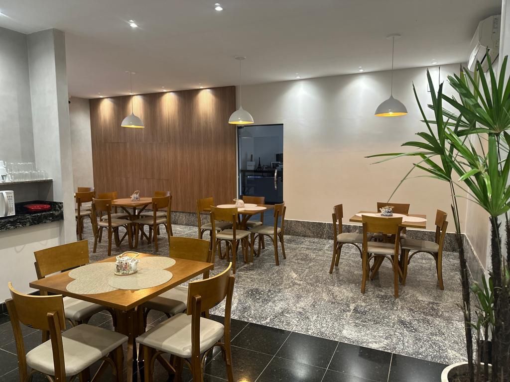 Interior de restaurante com mesas, cadeiras e iluminação suspensa. Paredes de madeira em tons claros