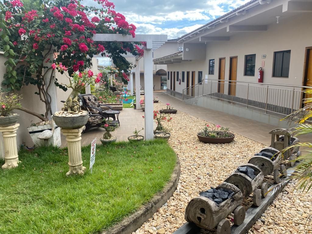 Um edifício com uma passarela, ladeado por uma área gramada com uma escultura de trem e um jardim de flores.