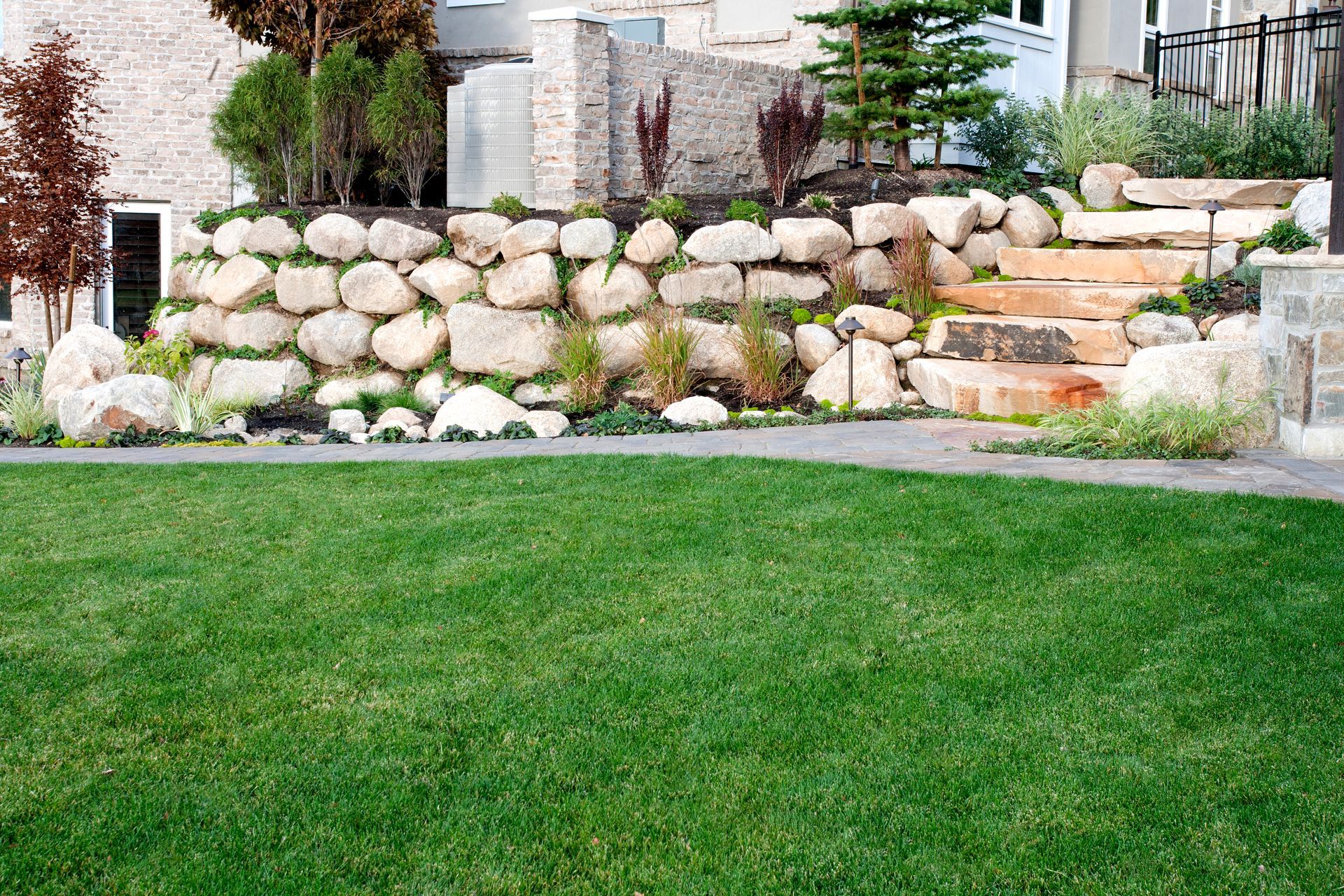 A lush green lawn with a stone wall and stairs in front of a house.