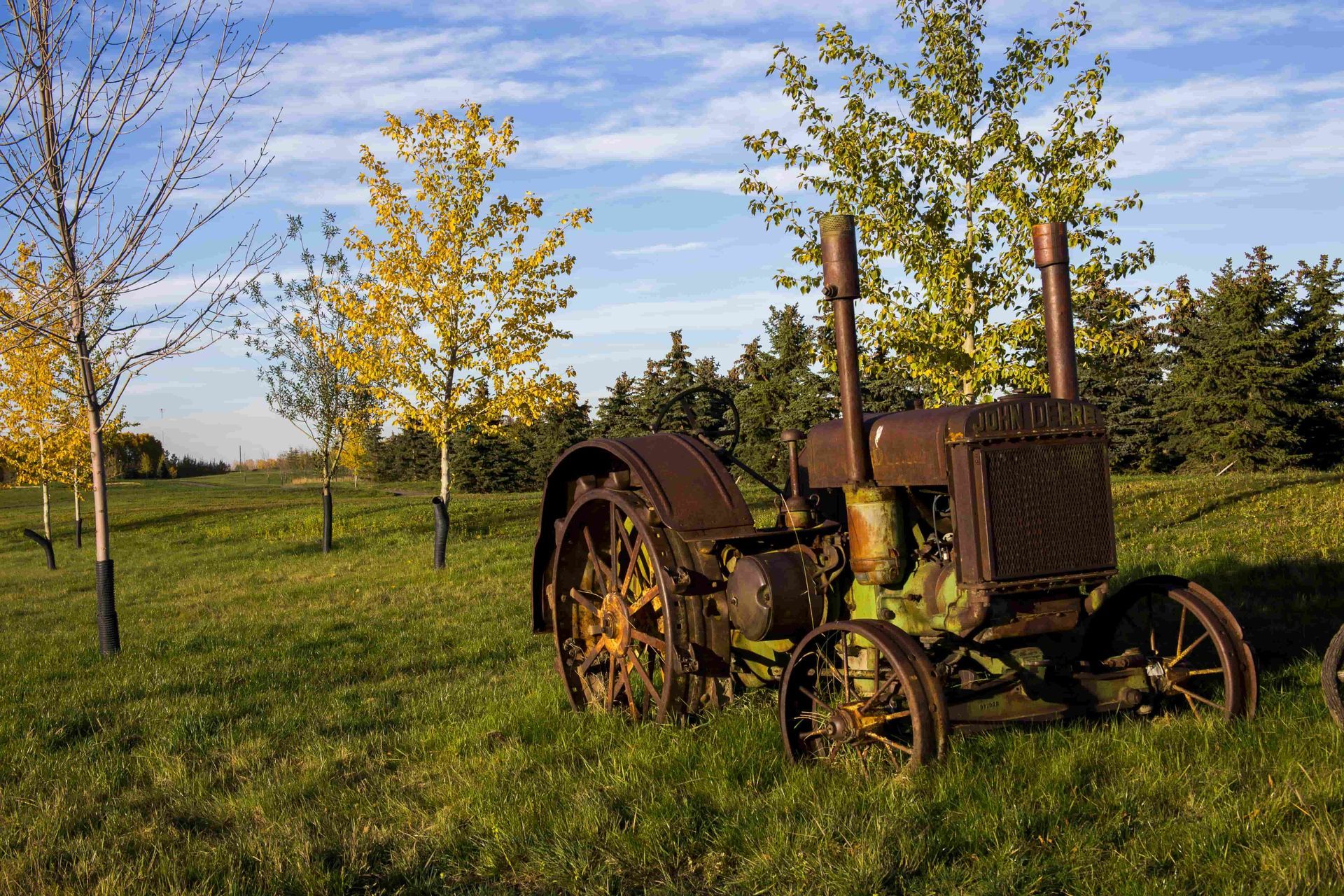 Old rusty tractor in a grassy field with trees under a blue sky.