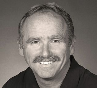 Man with mustache smiling, wearing dark shirt.