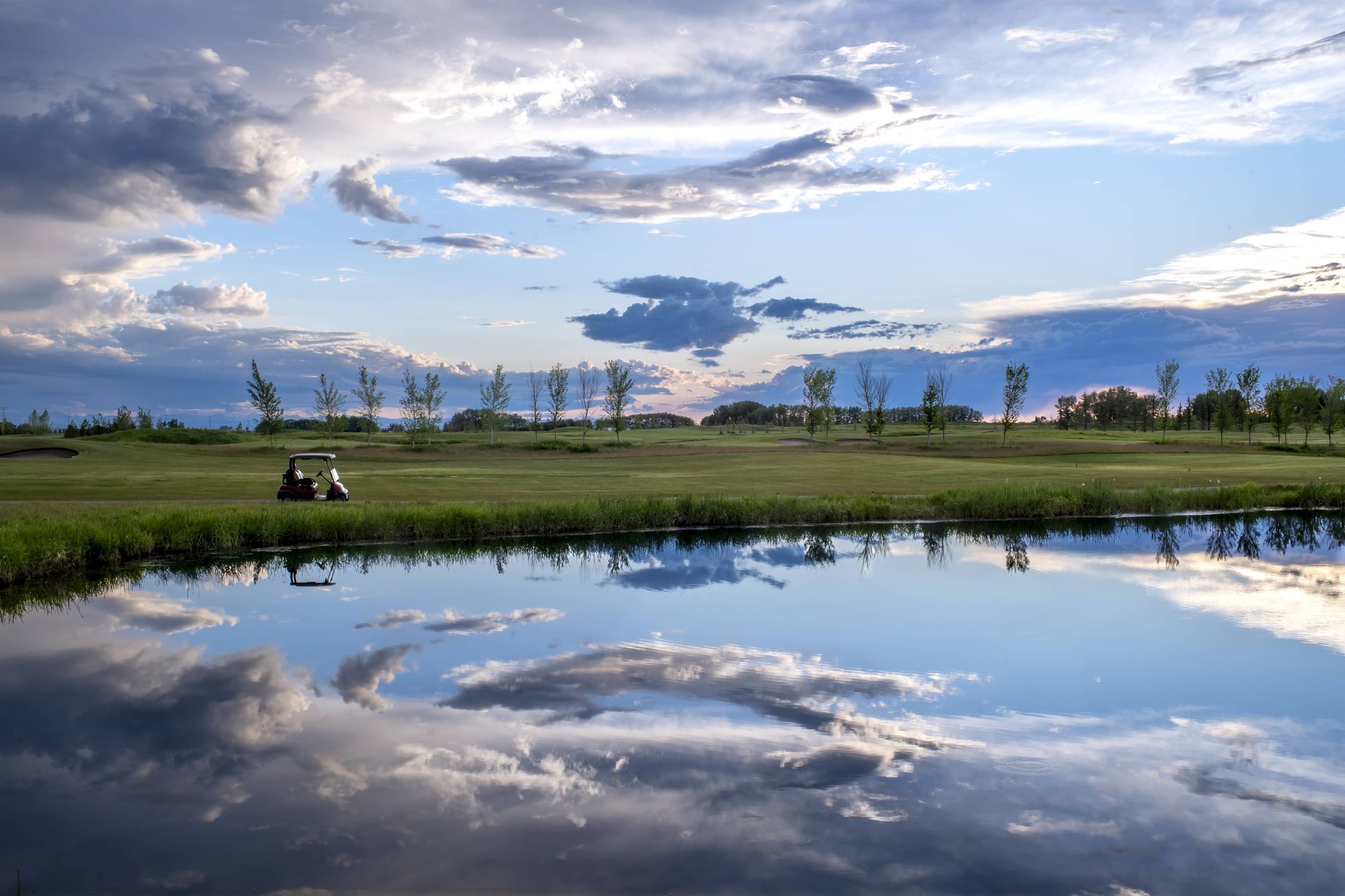 Golf course landscape with reflective water, golf cart, and cloudy sky.