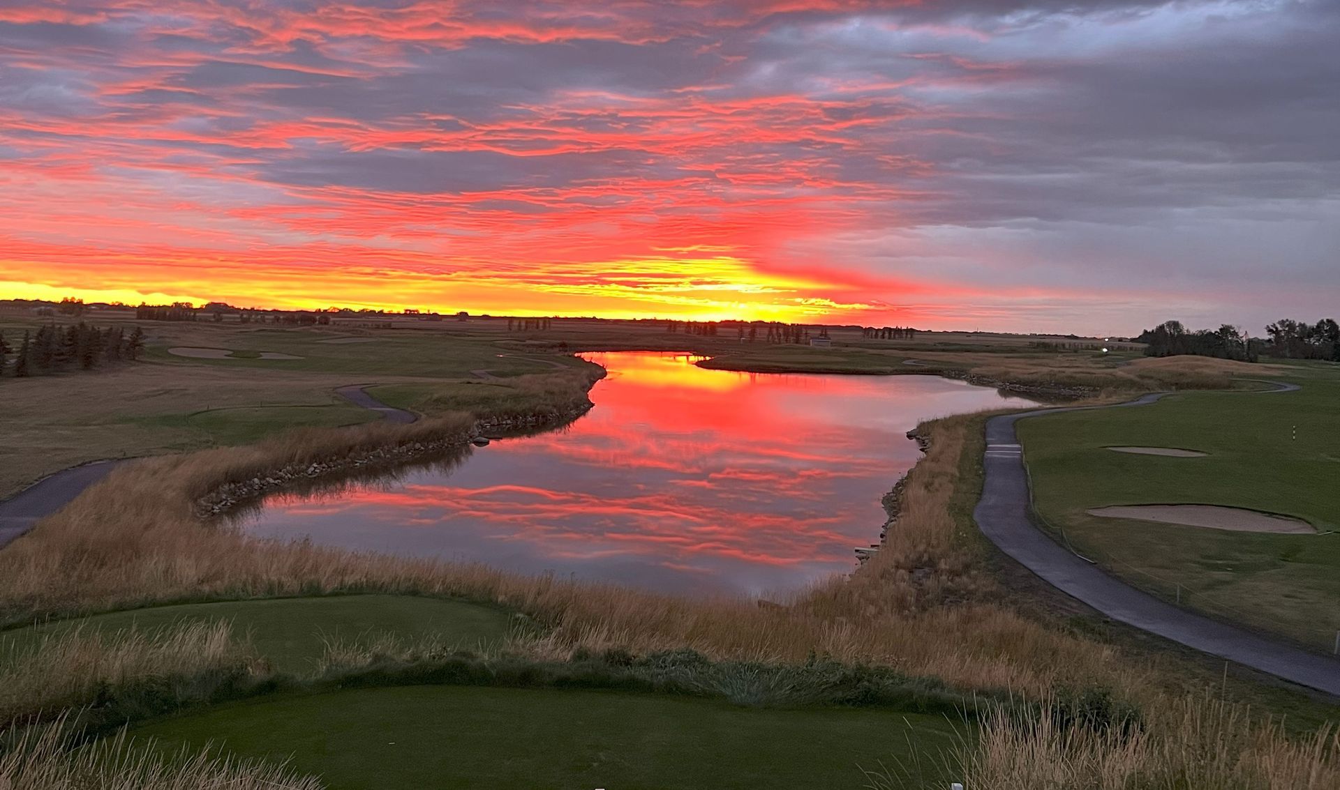 Golfer swinging on a green golf course under a double rainbow.