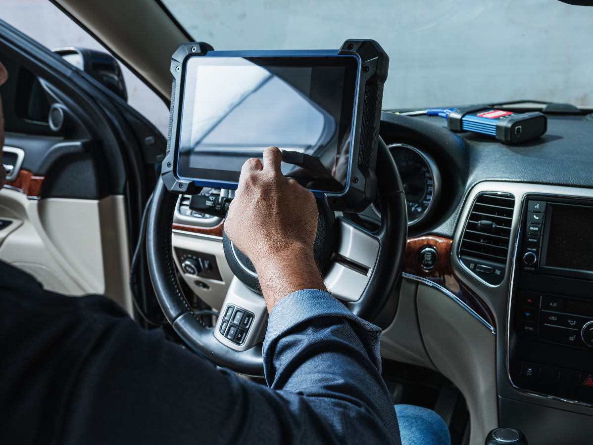 Mechanic using a tablet diagnostic tool inside a car, near steering wheel.