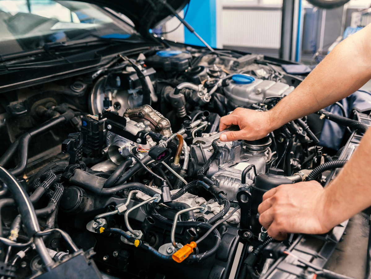 Mechanic's hands working on a car engine under the hood in a well-lit shop.