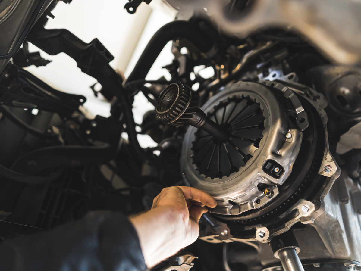 Mechanic's hand working on a car clutch inside the engine bay.