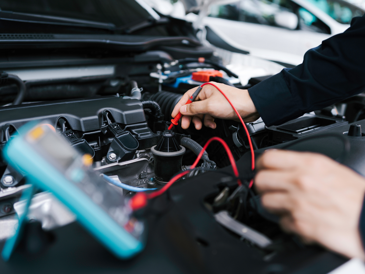 A mechanic uses a multimeter to inspect a car engine's electrical components.