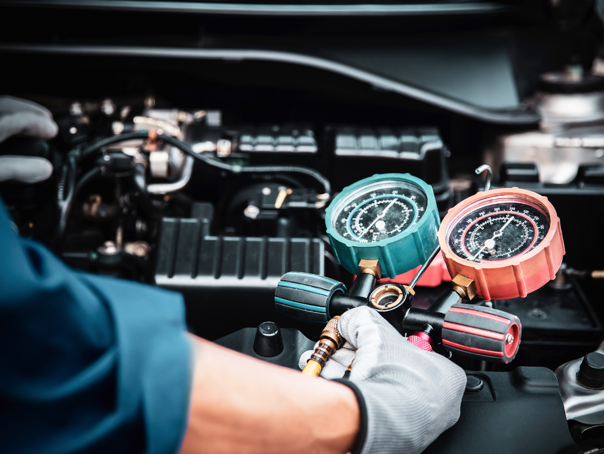 Mechanic using gauges to check car's air conditioning system in an engine bay.