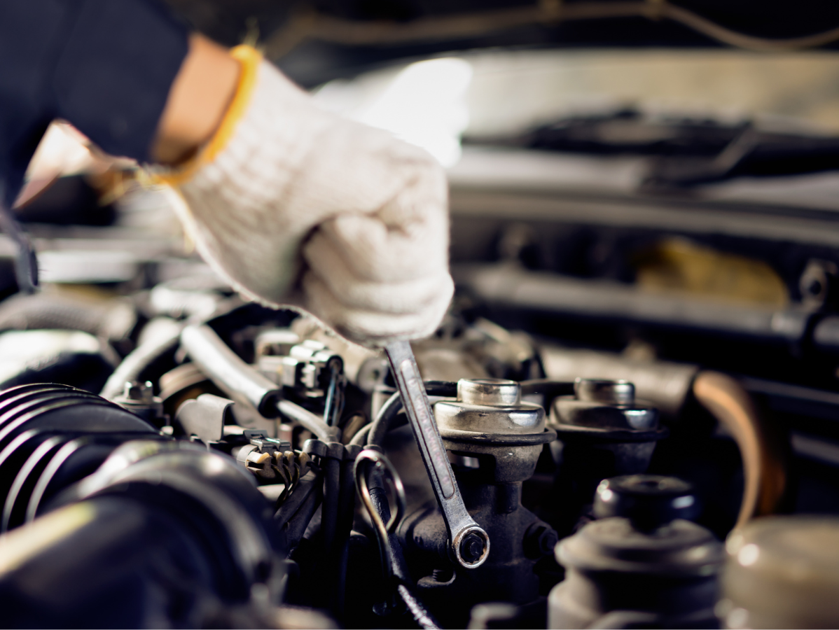 Mechanic's gloved hand using a wrench to work on a car engine in an engine bay.