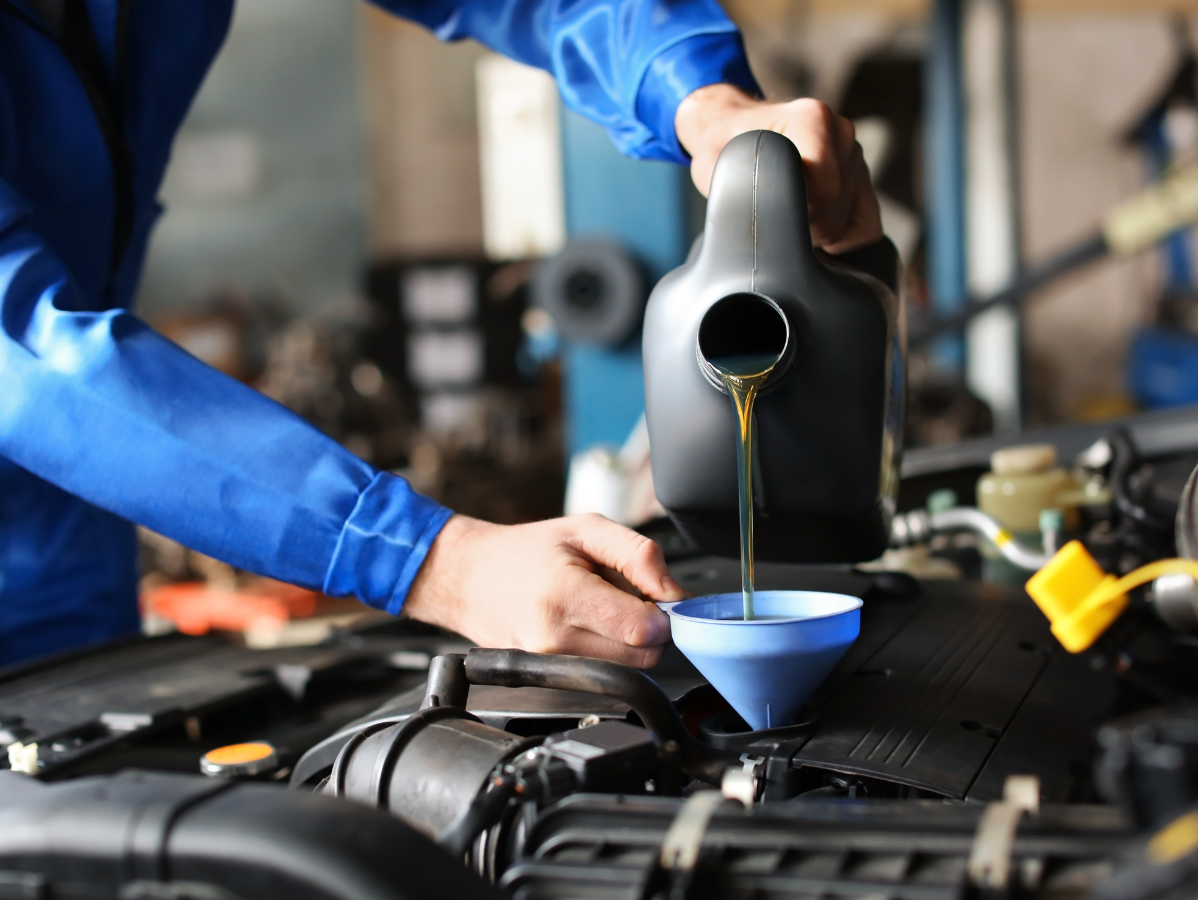 Mechanic pouring oil into a car engine, using a funnel.