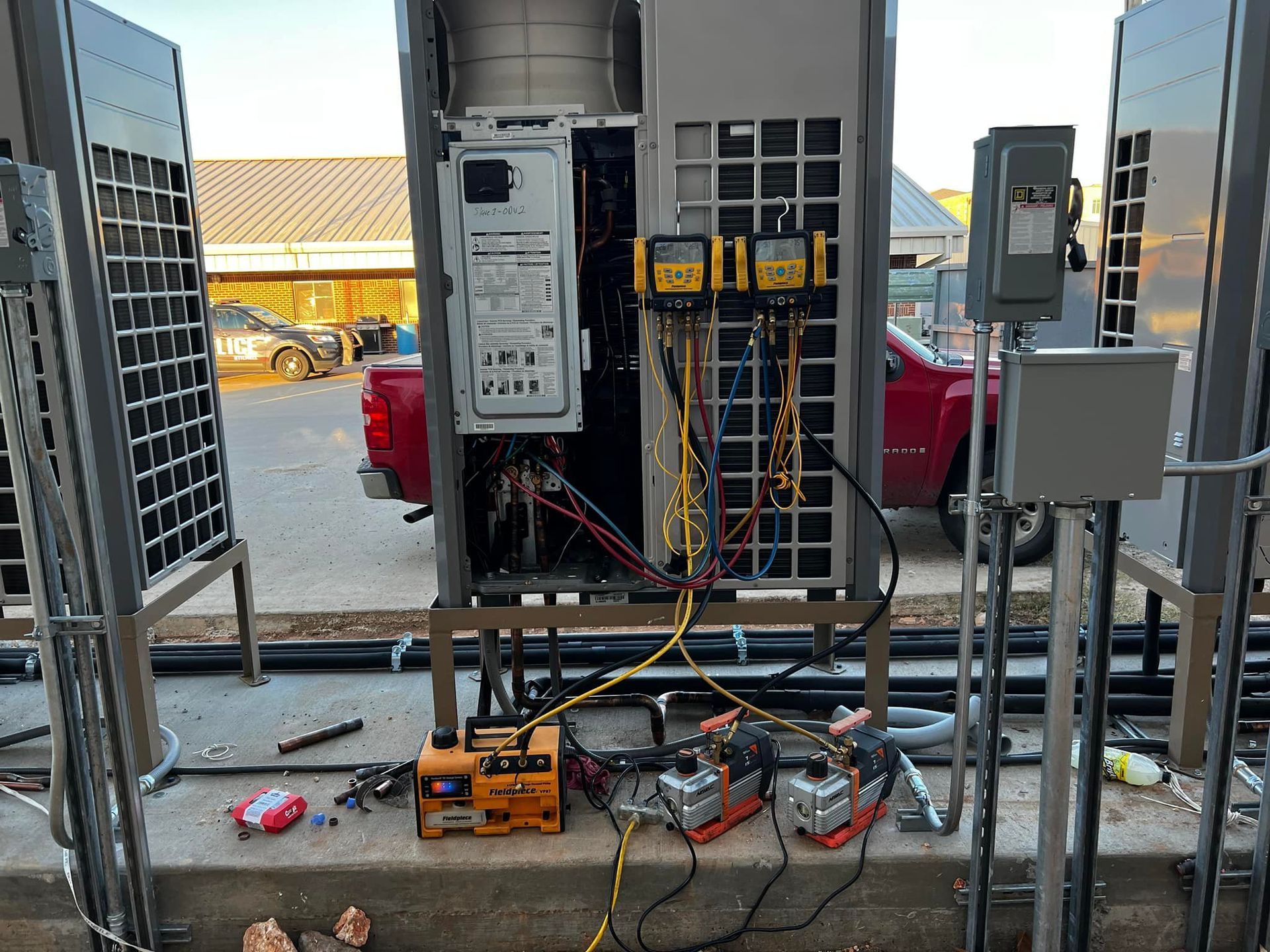 Electrical equipment being worked on outside; wiring and components visible. A red truck and buildings are in the background.
