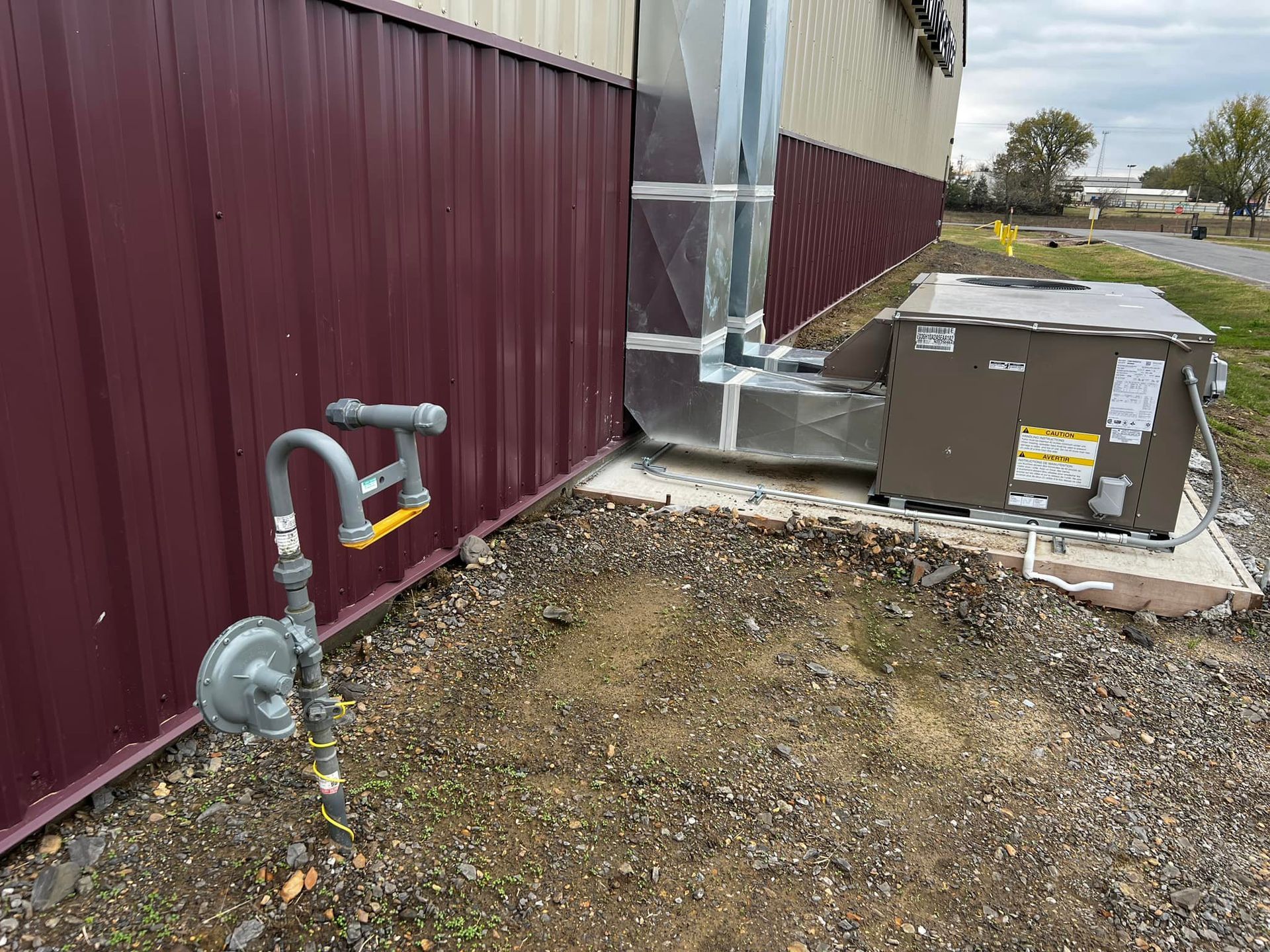 Exterior view of a building with a maroon wall, natural gas meter, and HVAC unit. 