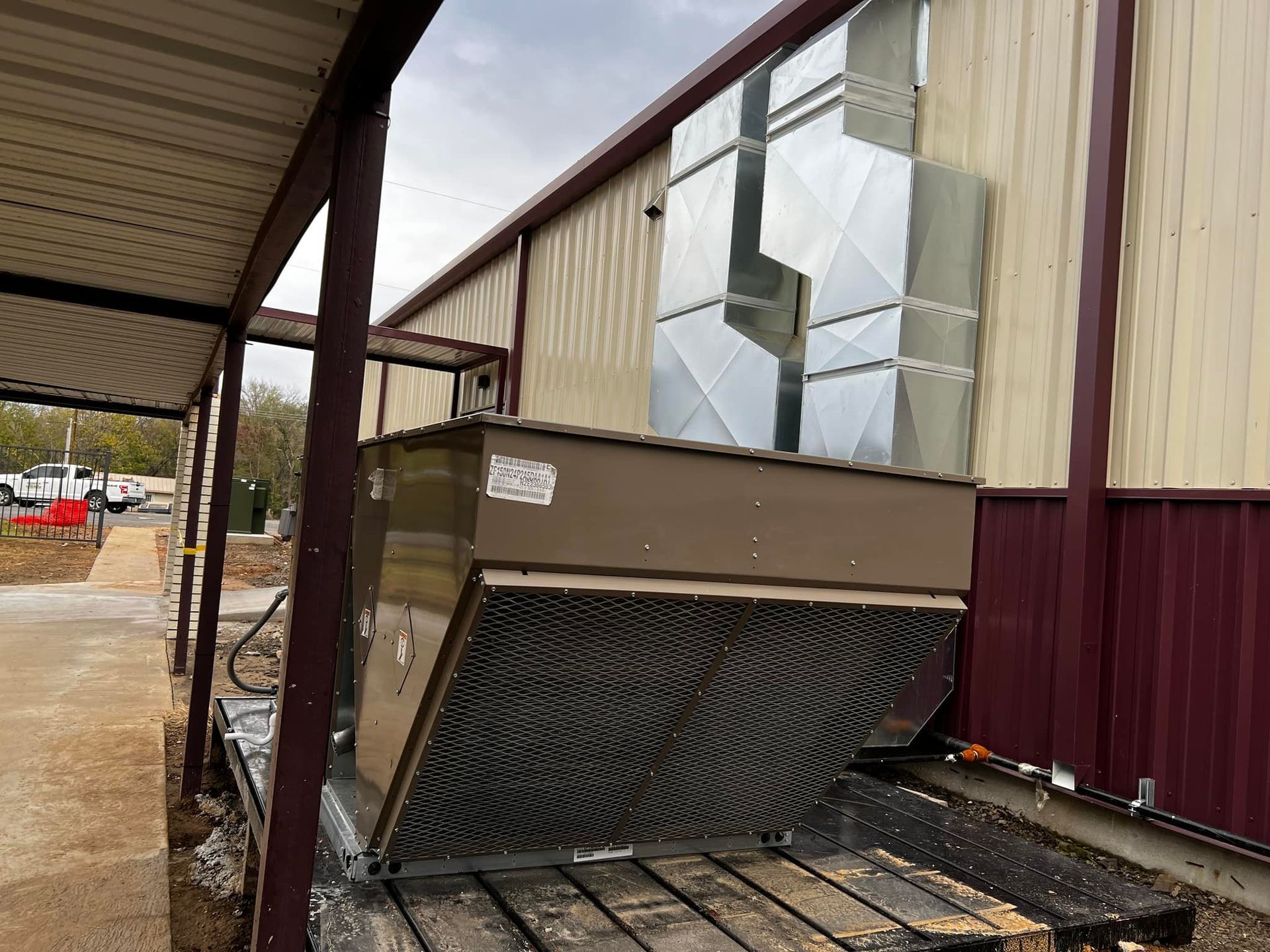 Brown industrial air conditioning unit outside a metal building with ductwork and a covered walkway.