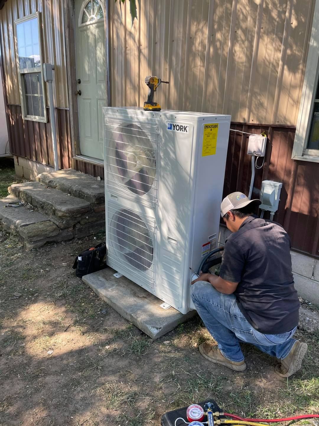 A person in jeans installing an air conditioning unit outside a building with a beige facade.