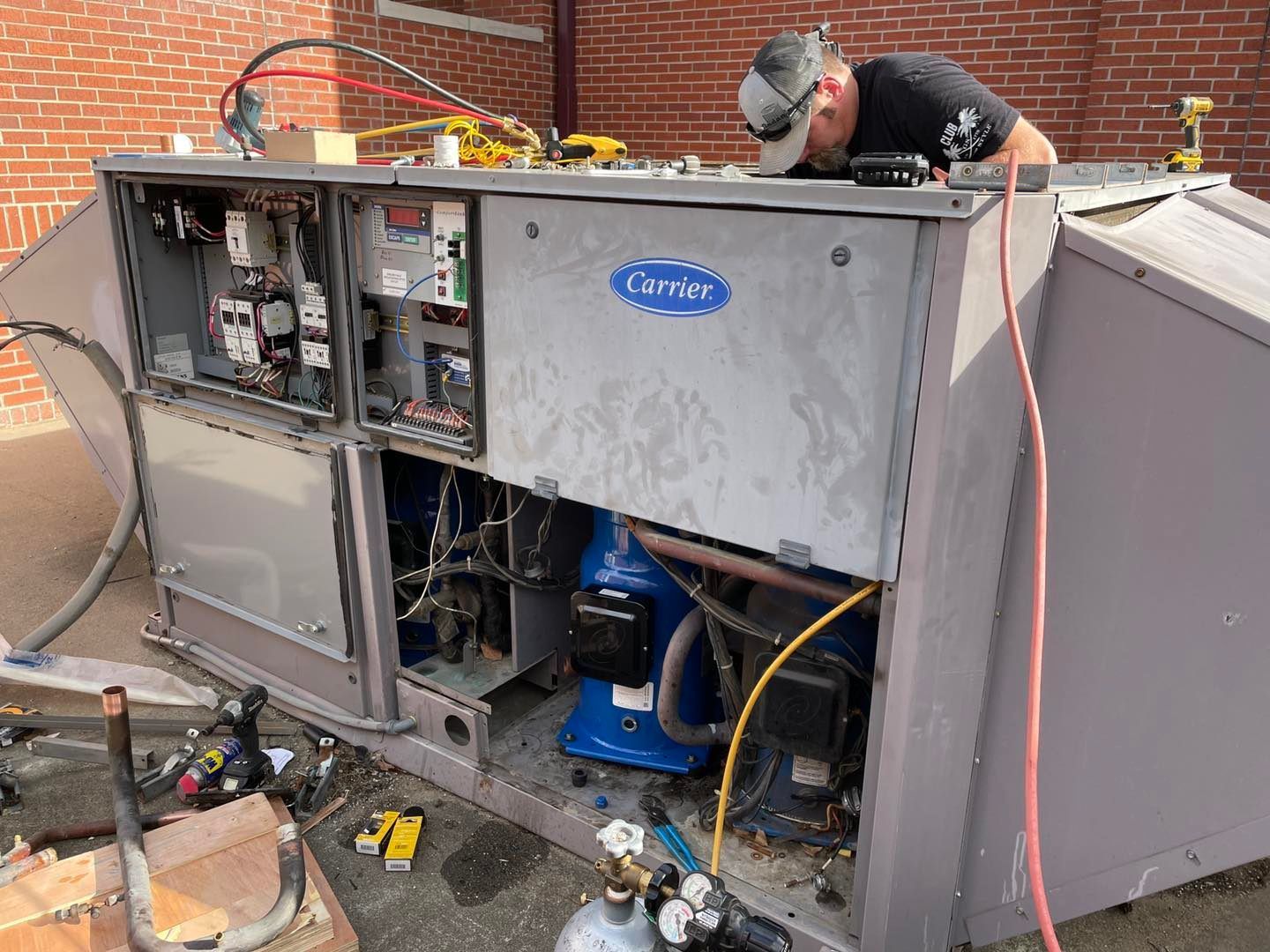A man works on a Carrier rooftop HVAC unit. The unit is open, revealing electrical components and the compressor.