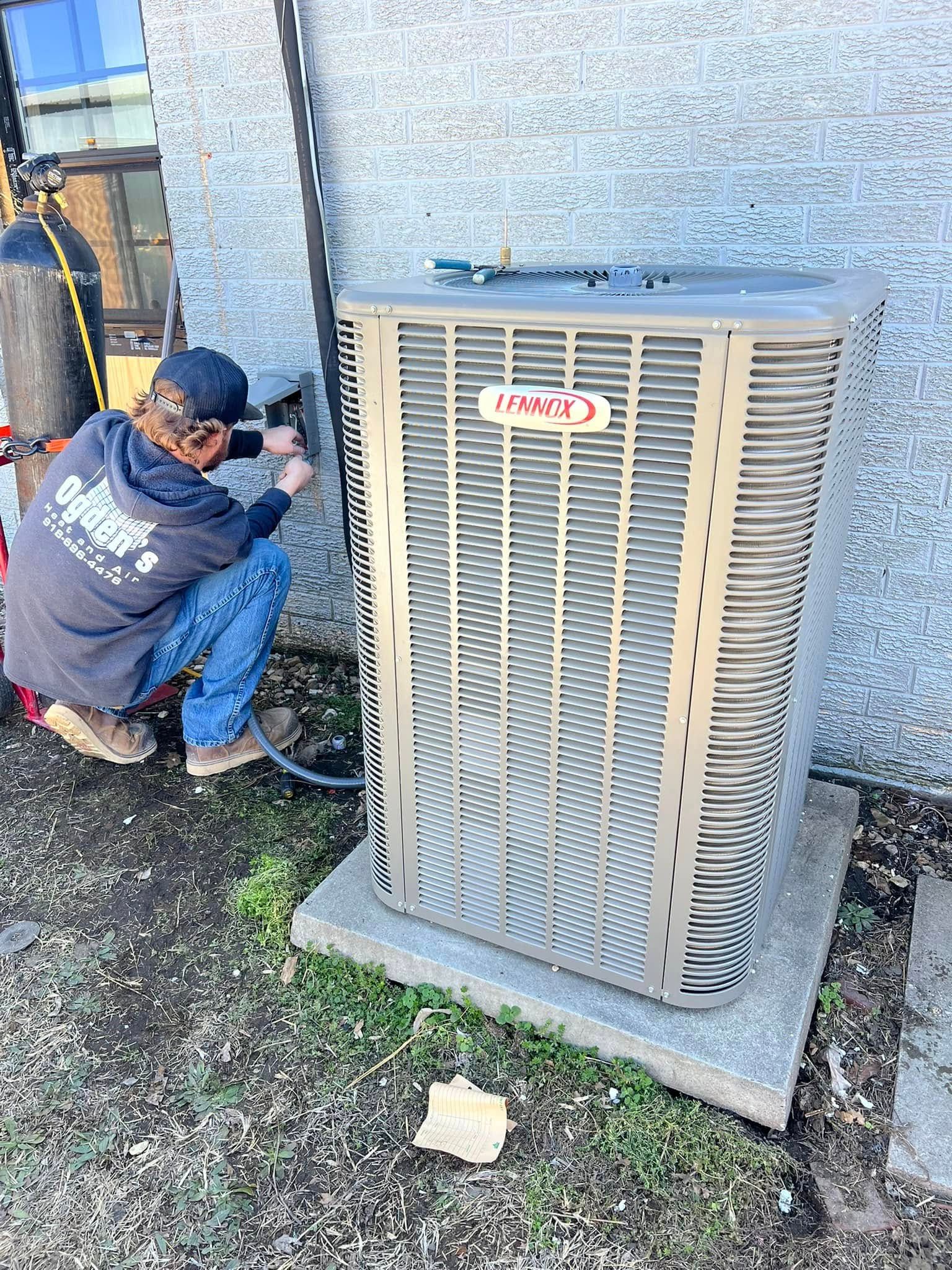 HVAC technician working on an outdoor air conditioner unit. He's kneeling near the unit, next to an oxygen tank.