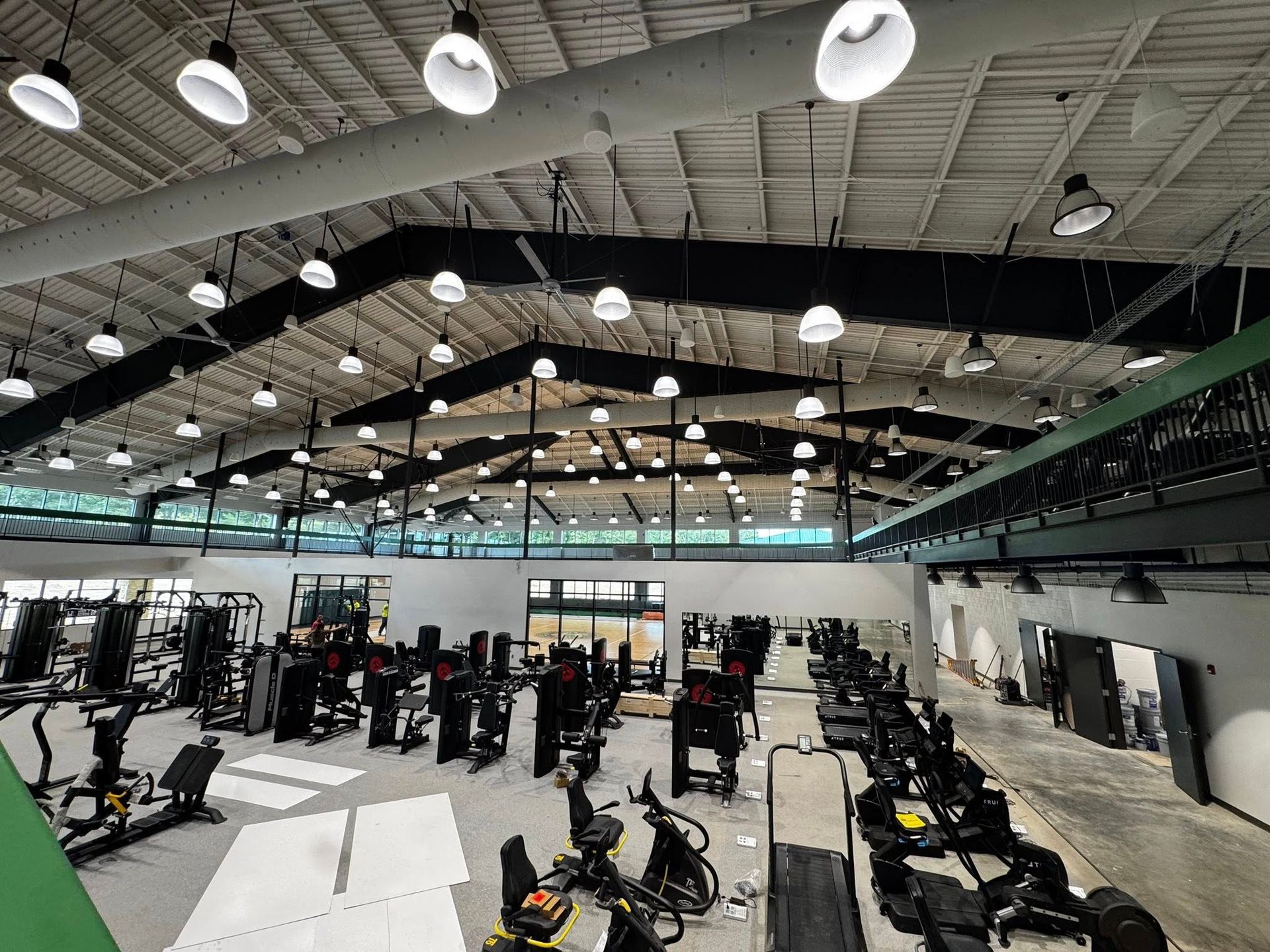 Interior view of a spacious gym with workout equipment, bright overhead lights, and a high ceiling.