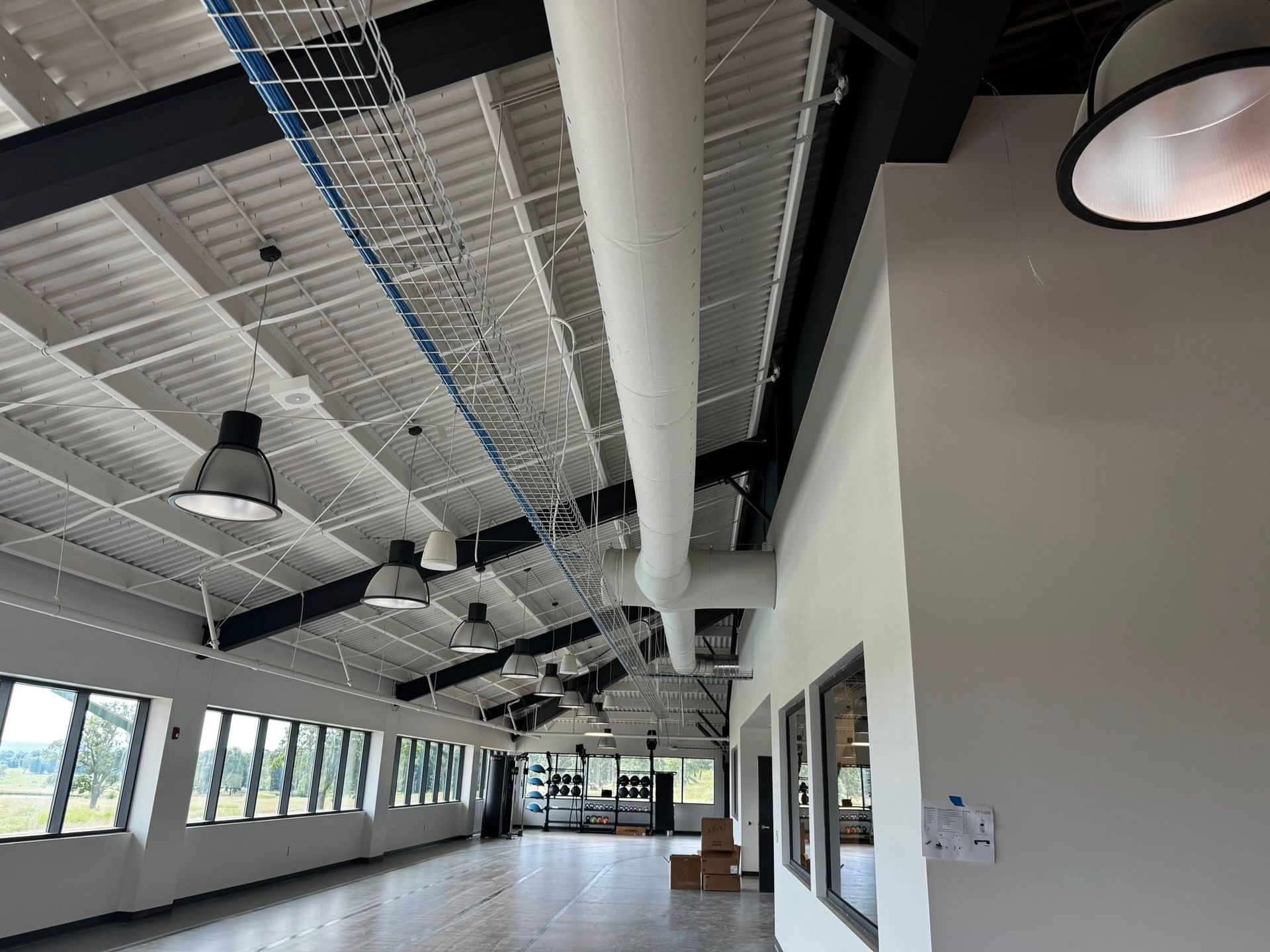 Interior of a long, open space with a white corrugated metal ceiling, black beams, and large windows.