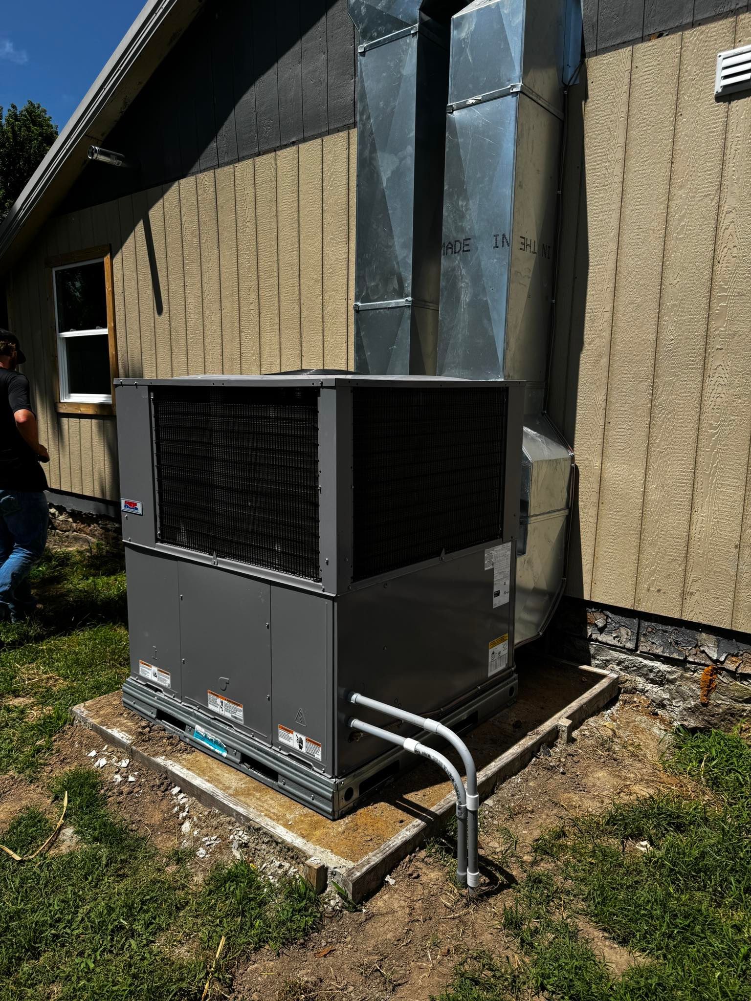 An outdoor air conditioning unit with ductwork attached to a building's side.