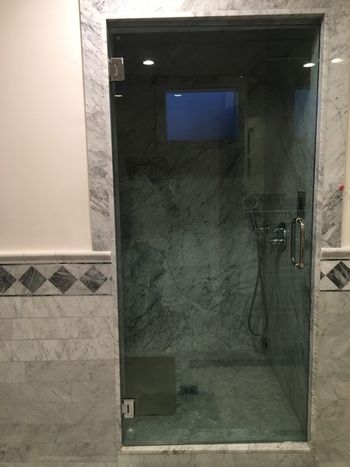 A bathroom with a glass shower door and a marble wall.