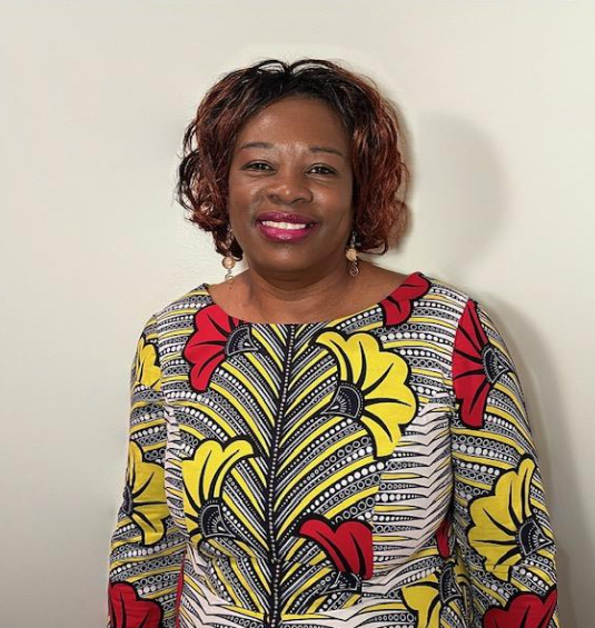 A woman wearing a yellow and red floral shirt is smiling for the camera.