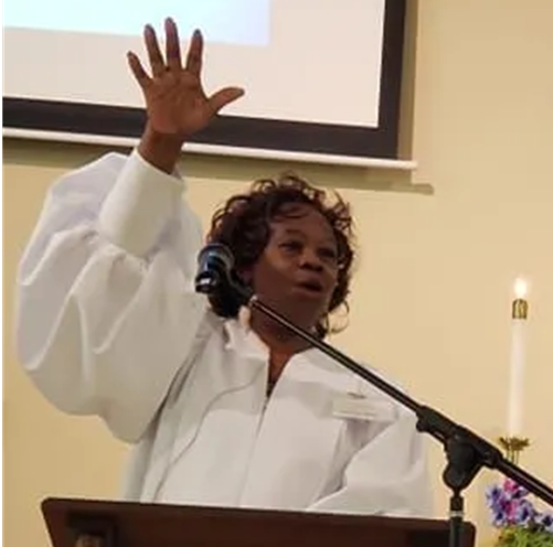A woman in a white robe is standing at a podium with her hand in the air.