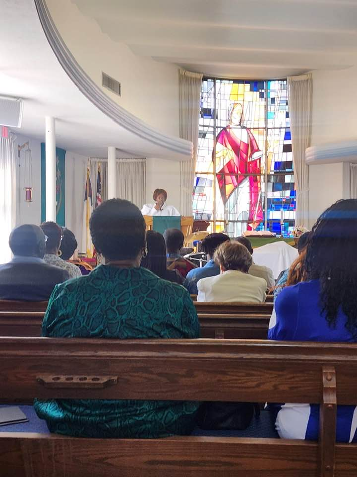 A group of people are sitting in a church with a stained glass window in the background
