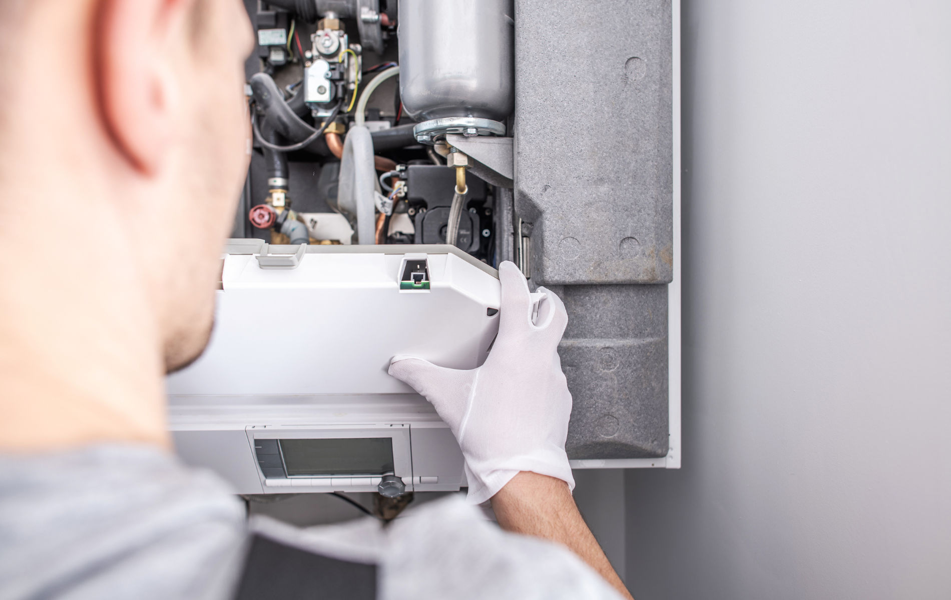 A man wearing white gloves is working on a boiler.