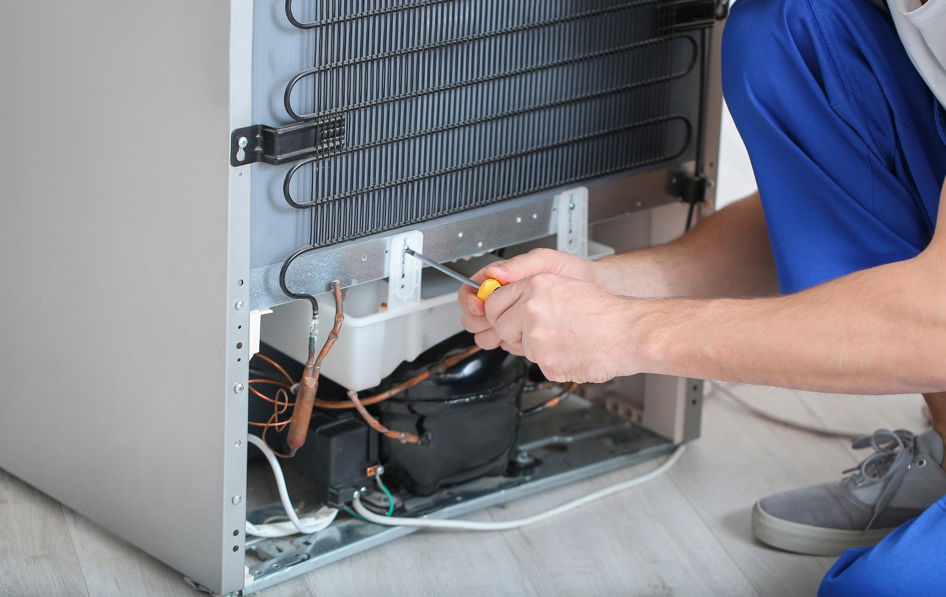A man is fixing a refrigerator with a screwdriver.