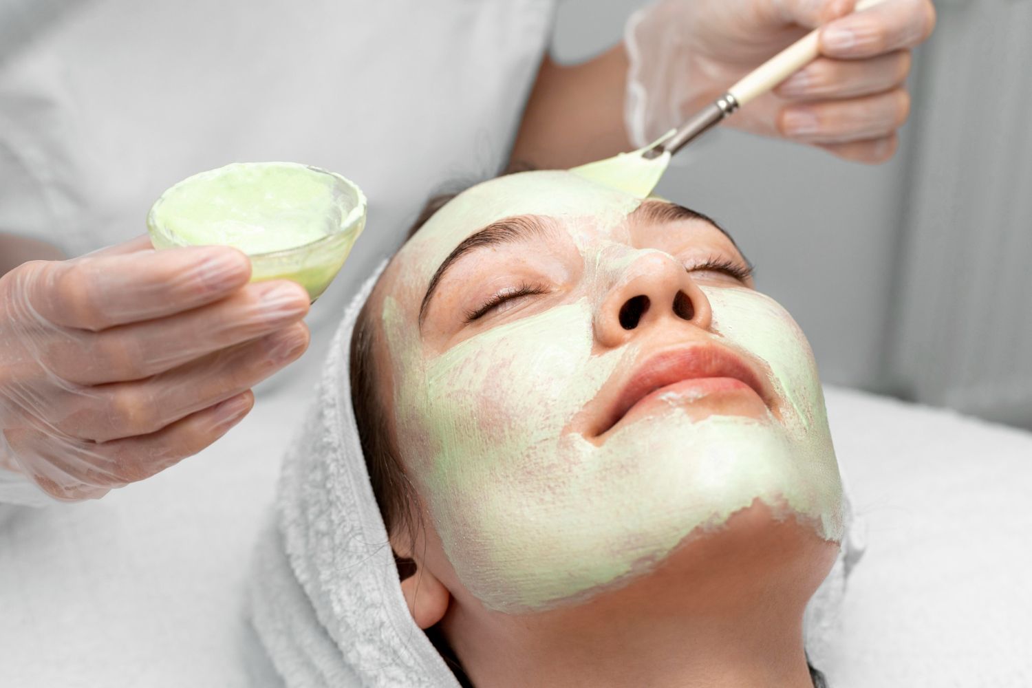 A woman is getting a green mask on her face.