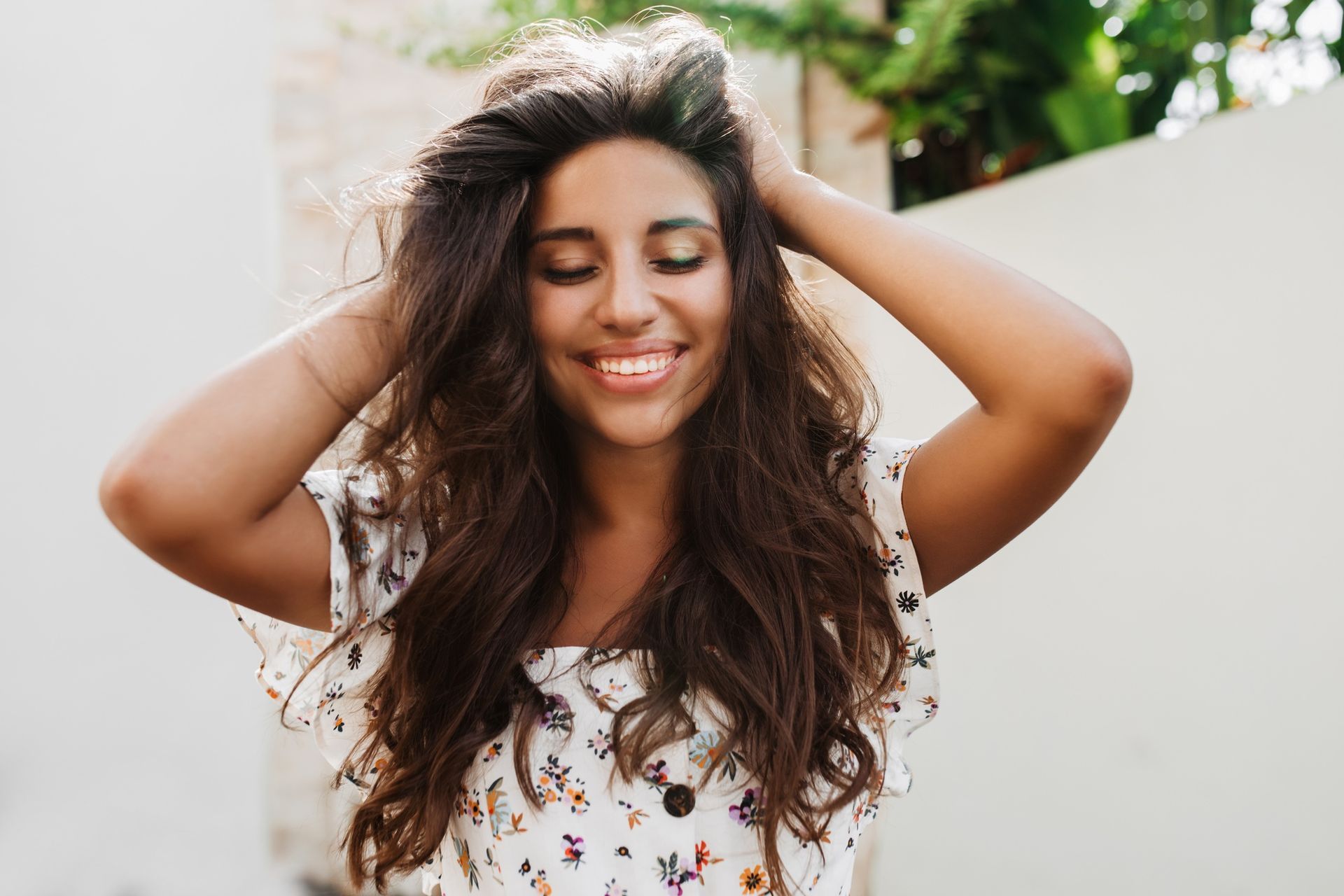 A woman with long hair is smiling and holding her hair in her hands.