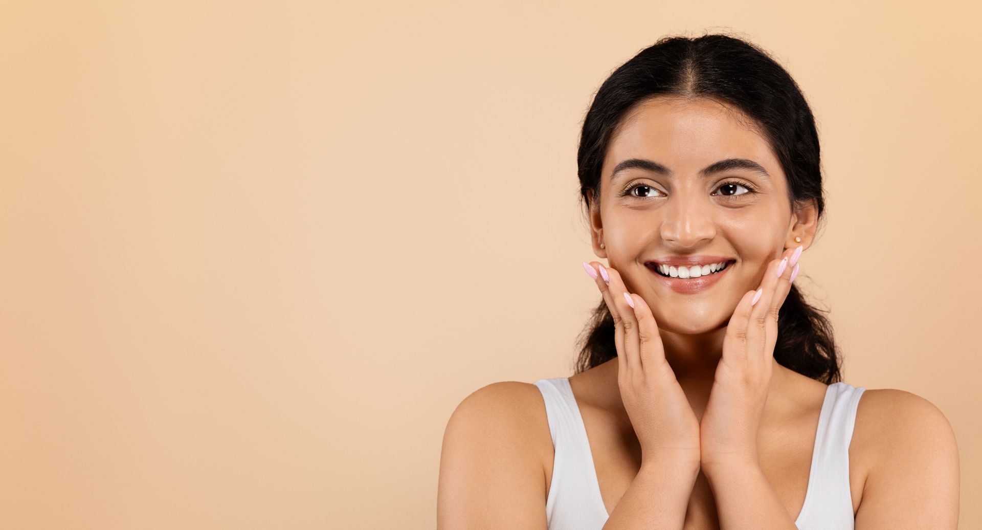 A woman is smiling and touching her face with her hands.