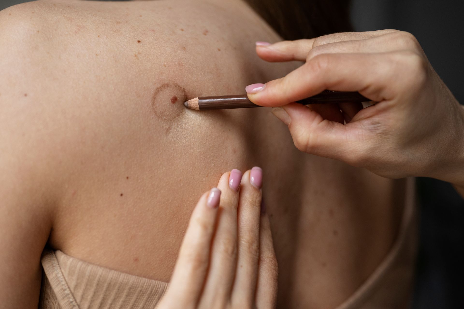 A woman is applying makeup to another woman 's back with a pencil.