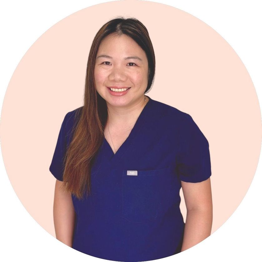 A woman in a blue scrub top is smiling for the camera.