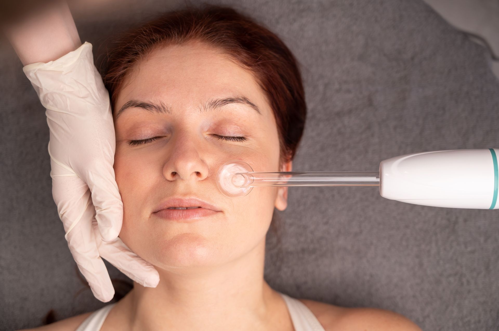 A woman receiving a high-frequency facial treatment with a handheld device at a clinic
