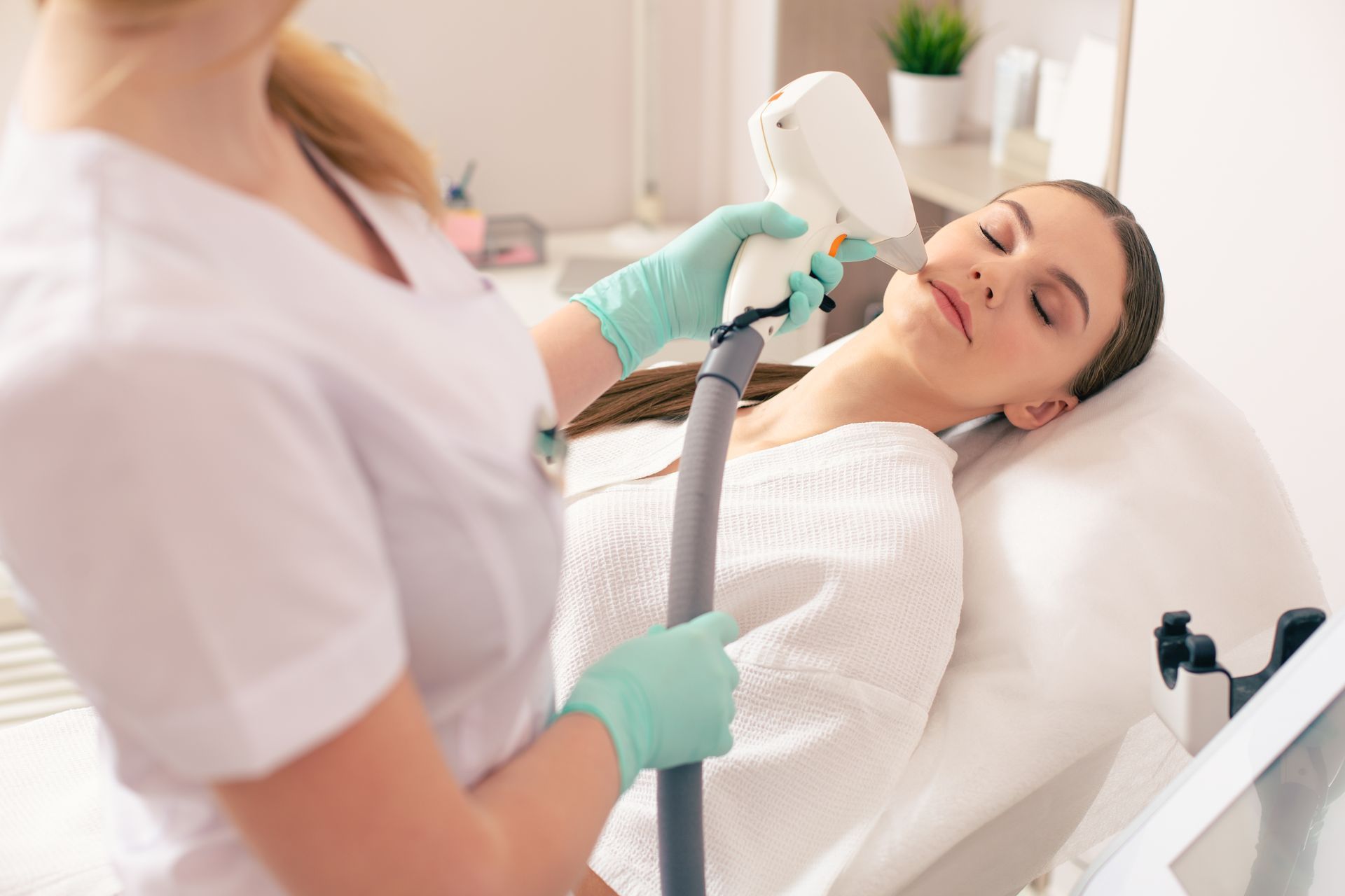 A medical professional performing laser skin treatment on a woman's face in a clinic.