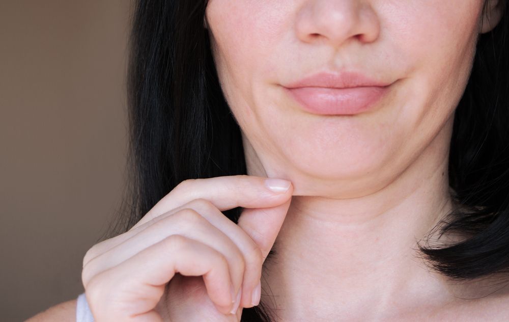 Woman holding skin under chin, creating double chin.