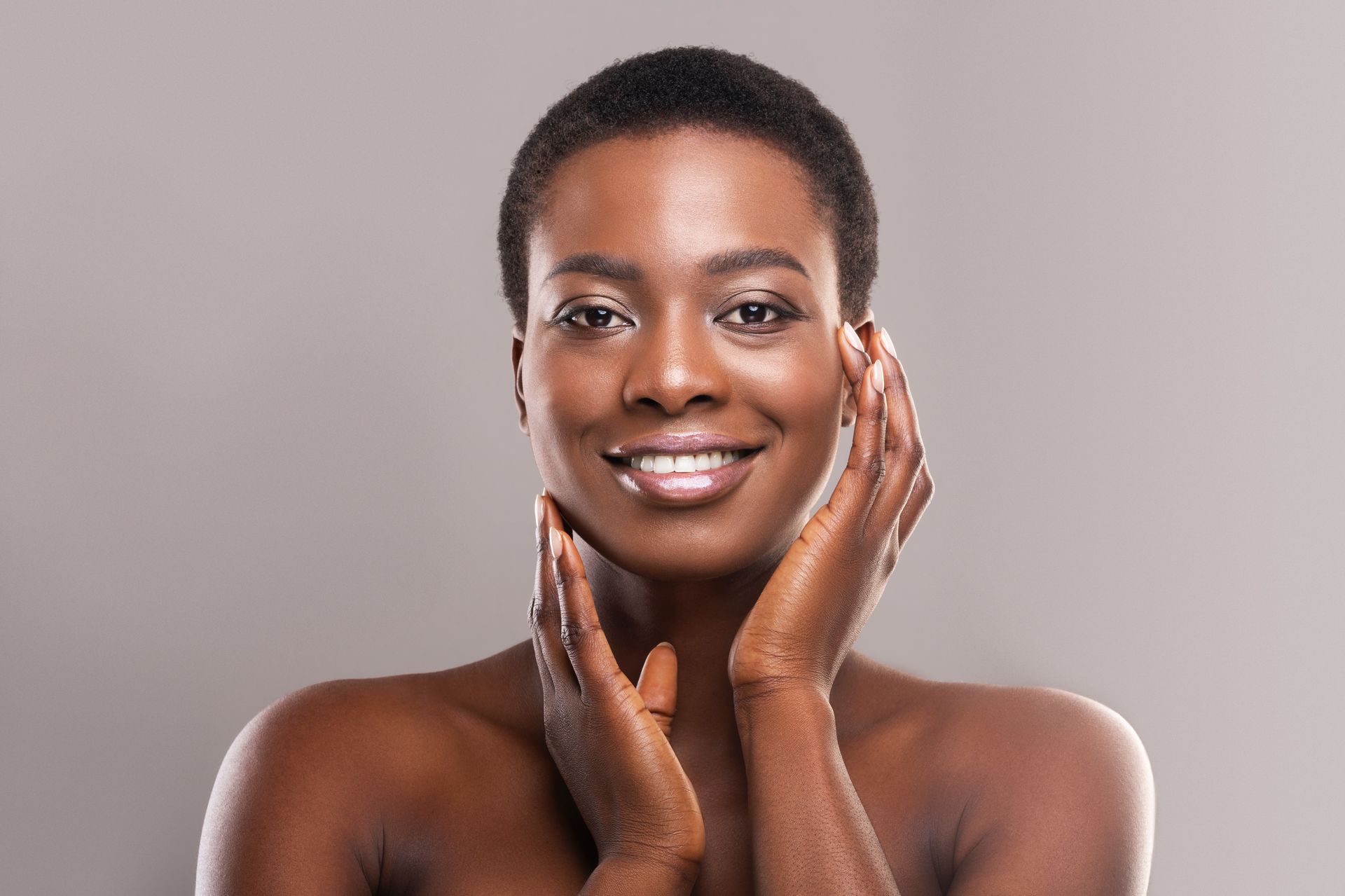 A woman is smiling and touching her face with her hands.