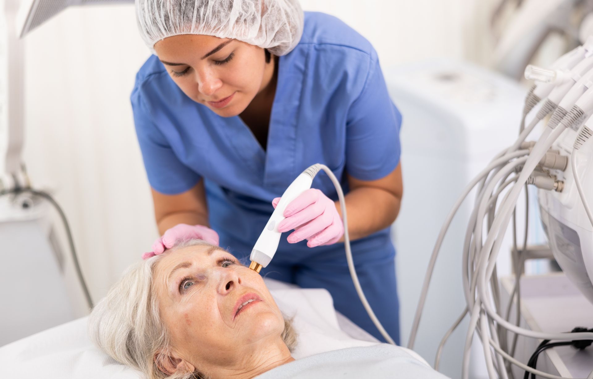 A medical professional in blue scrubs performs a cosmetic procedure on a patient's face, using a handheld device.