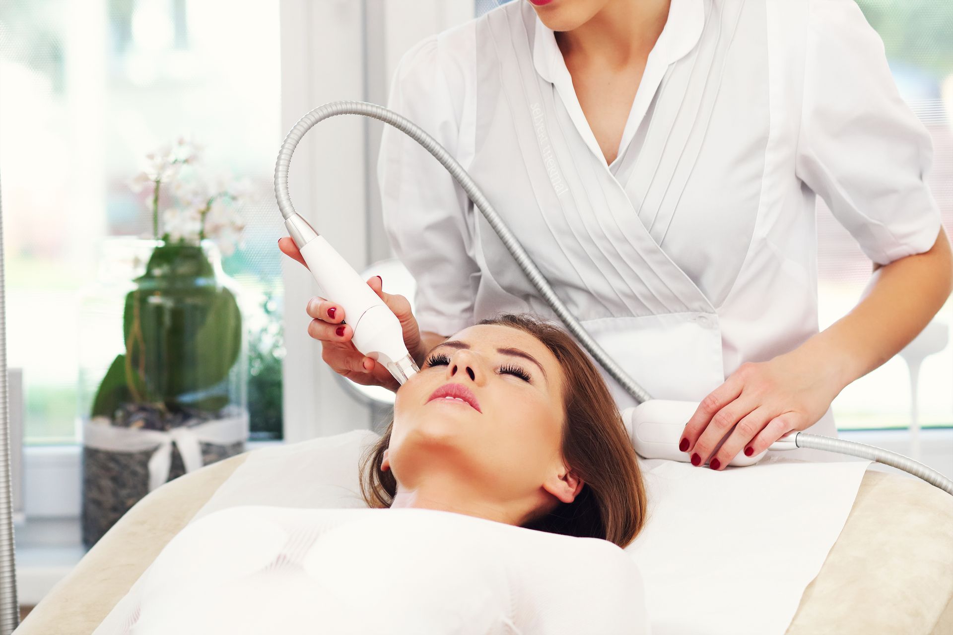 Woman receiving facial treatment in a salon. A esthetician uses a wand to apply a procedure.